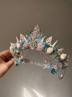 a hand holding up a tiara with seashells, pearls and other items