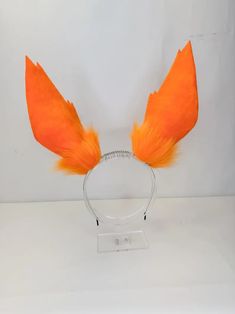 an orange feathered headband is displayed on a white surface with clear acrylic