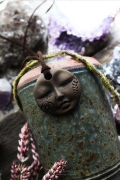 a clay face is placed on the top of a metal container next to some flowers