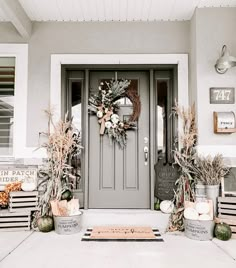 a front door decorated for fall with pumpkins, corn stalks and wreath on it