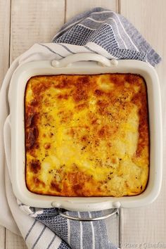 a square casserole dish with cheese and herbs in it on a striped towel