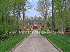 a driveway leading to a large brick house surrounded by trees and grass in front of it