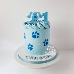 a blue frosted birthday cake with dog paw prints on the top and one candle in the middle