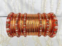 The perfect fusion of tradition and style, designed to elevate your outfit with elegance and charm. This stunning bangle set offers the versatility you've been searching for, as it can be tailored to adorn either one hand or both, ensuring that you shine in any setting. This set includes a total of 24 colored bangles, carefully selected to complement a wide range of outfits and moods. 2 stunning Kara bangles add a touch of mystique and allure to your ensemble, and 4 Churi bangles provide a captivating contrast to your look. To maintain a balance we've also included 11 plain insert bangles, offering a clean and classic finish to your overall aesthetic. Bangles Indian, Crystal Bangle, Bangle Set, Orange Gold, Indian Jewellery, Gold Bangles, Gold And Silver, Indian Jewelry, Dark Pink