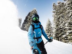 a person riding skis down a snow covered slope with trees in the back ground