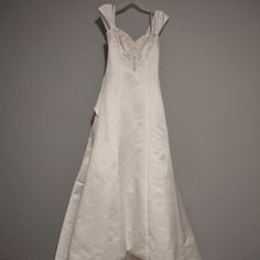 a white wedding dress hanging on a hanger in a room with gray walls and flooring