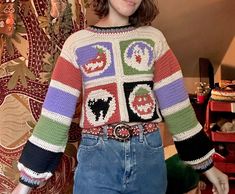 a woman standing in front of a wall wearing a multicolored sweater and jeans