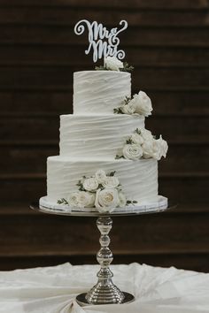 a white wedding cake sitting on top of a glass stand with flowers and the words mr and mrs written on it