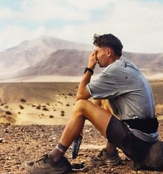 a man sitting on the ground with his hand to his face and looking off into the distance