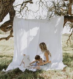 a woman sitting on the ground next to a child in front of an easel