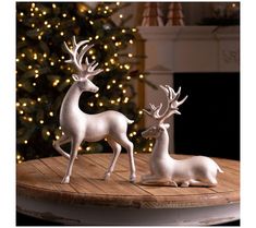 two white deer figurines sitting on top of a wooden table next to a christmas tree