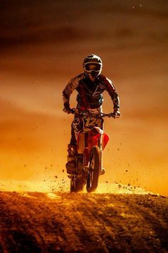 a man riding a dirt bike on top of a dirt covered hill at night time