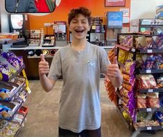 a young boy standing in front of a store holding up his thumb and giving the thumbs up