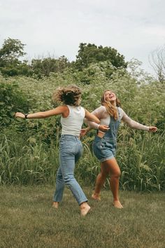 two young women are playing with a frisbee in the grass near some tall grass