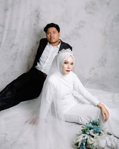 a man sitting next to a woman in a white dress and veil on her head