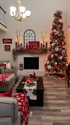 the living room is decorated for christmas with red and white decorations on the tree, fireplace, and couches