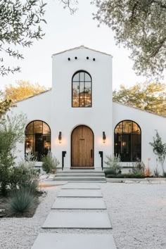 a white house with two doors and steps leading up to the front door is surrounded by greenery