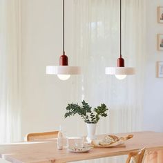 a dining room table with two hanging lights above it and a potted plant in the center