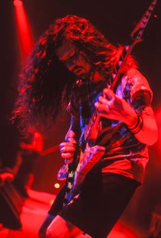 a man with long hair holding a guitar in his hand and standing on stage at a concert