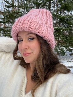 a woman wearing a pink knitted hat in front of snow covered ground and trees