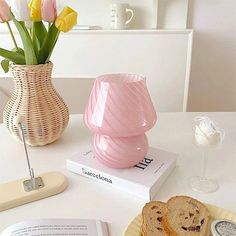 a pink vase sitting on top of a table next to a book and some bread