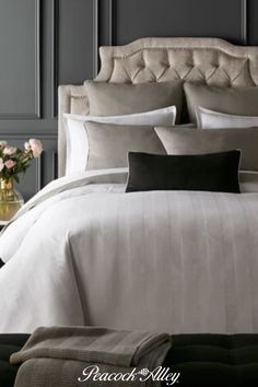 a bed with white sheets and pillows in a bedroom next to a vase filled with flowers