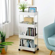 a white book shelf with books on it in a room next to a blue chair and potted plant