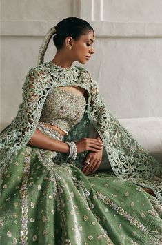 a woman in a green gown sitting on a couch wearing jewelry and a tiara