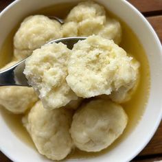 a white bowl filled with dumplings sitting on top of a wooden table next to a spoon