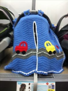 a crocheted blue backpack with cars on the front and sides, sitting on a shelf