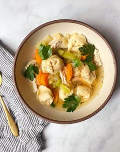 a bowl filled with dumplings, carrots and celery next to a spoon