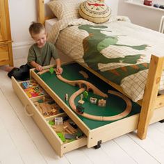 a young boy playing with his toy train set on the floor in front of a bed