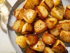 a white plate topped with cooked potatoes next to a glass of wine