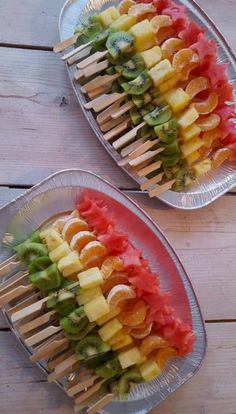 two trays filled with fruit and skewers on top of a wooden table