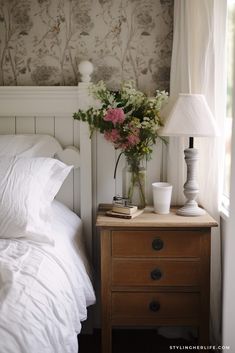 a nightstand with flowers on it next to a bed