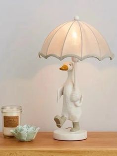 a white duck holding an umbrella on top of a table next to a cup and candle