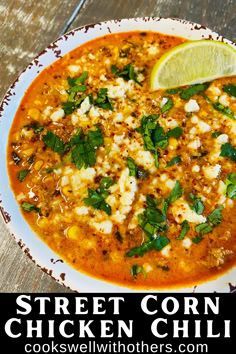 a white bowl filled with chicken chili and garnished with cilantro, cheese, and lime