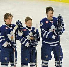 three young men standing next to each other on top of an ice rink holding hockey sticks