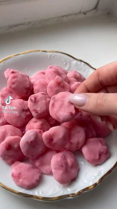 a hand is picking up some pink candy from a white and gold plate on a table