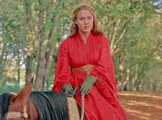 a woman riding on the back of a brown horse in a red dress and green gloves