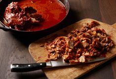 a wooden cutting board topped with meat next to a skillet filled with red sauce