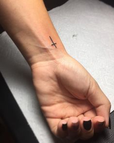 a woman's hand with a small cross tattoo on her left wrist and black nails