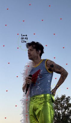 a man in green pants holding a microphone and standing next to a tree with hearts on it