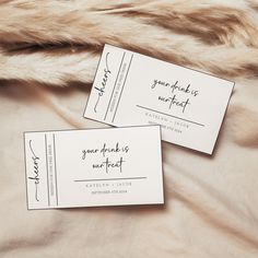 two white business cards sitting on top of a fur covered bed next to each other