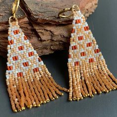 a pair of earrings with beaded fringes on top of a piece of wood