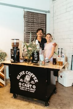 two women are standing behind a coffee cart