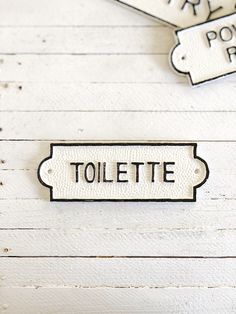 two tags that say toilet and one has a name tag attached to it on a white wooden surface