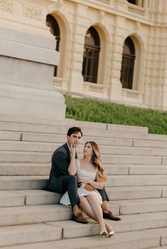 a man and woman sitting on the steps in front of a building, one holding her hand up to her face