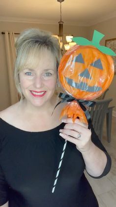 a woman holding up a pumpkin balloon in her hand with a stick sticking out of it