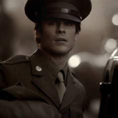 a man in uniform is standing next to a car and looking at the camera with an intense look on his face